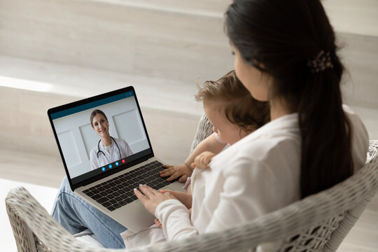 Loving mother hugging holding baby little daughter, using laptop, making video call to female pediatrician at home, doctor consulting caring mom online, telemedicine and children healthcare concept