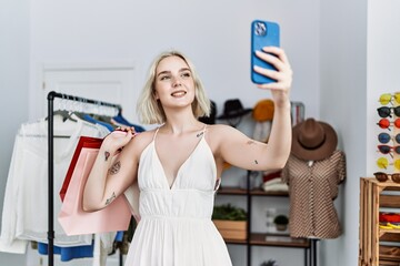 Young caucasian woman holding shopping bags make selfie by the smartphone at clothing store