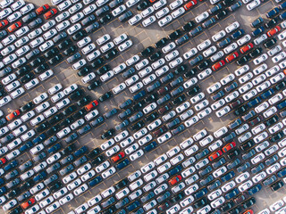 New multi-colored passenger cars are standing in straight diagonal rows in a giant parking lot on the territory of the plant, aerial view
