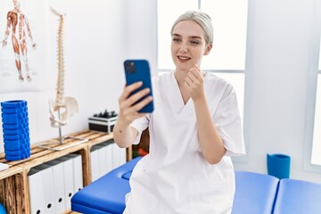 Young caucasian woman wearing physio therapist uniform having video call at clinic