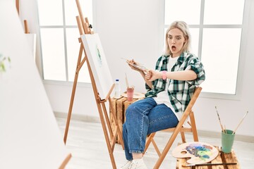 Young artist woman painting on canvas at art studio looking at the watch time worried, afraid of getting late