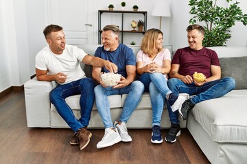 Group of middle age caucasian friends smiling happy watching movie at home.