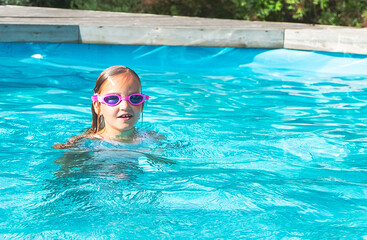 Fototapeta na wymiar Girl 6 years old, swims in the outdoor pool on a summer day. Sun glare.