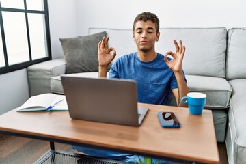 Young handsome hispanic man using laptop sitting on the floor relax and smiling with eyes closed doing meditation gesture with fingers. yoga concept.