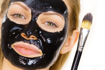 Woman applying black mud mask to face