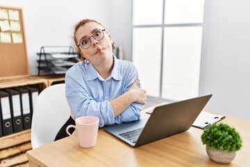 Young redhead woman working at the office using computer laptop making fish face with lips, crazy and comical gesture. funny expression.