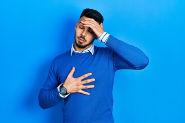Young hispanic man with beard wearing casual blue sweater touching forehead for illness and fever, flu and cold, virus sick