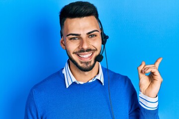 Young hispanic man with beard wearing operator headset at the call center office smiling happy pointing with hand and finger to the side