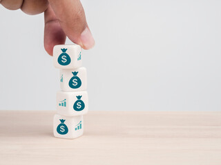 Hand put a white cube block with the dollar money bag icon symbol on the top of stack on white background with copy space. Increase budget, profits growth, investment funds and saving money concept.