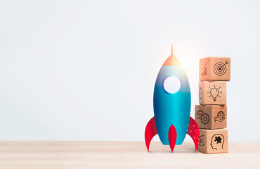 Business startup with growth success process for leadership concept. The rocket beside the wooden cube blocks stacks with business strategy icons on wooden table on white background with copy space.