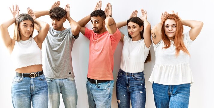 Group of young friends standing together over isolated background doing bunny ears gesture with hands palms looking cynical and skeptical. easter rabbit concept.