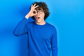 Fototapeta na wymiar Handsome young man wearing casual clothes and glasses doing ok gesture shocked with surprised face, eye looking through fingers. unbelieving expression.