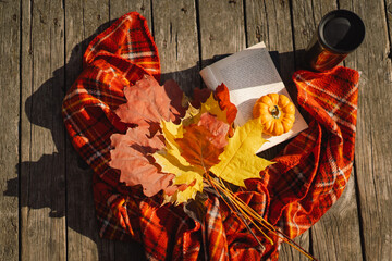 Open book with orange pumpkin, bouquet of autumn leaves with a plaid on a wooden background. Autumn mood. Read and rest. Cozy autumn concept.