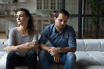 Depressed unhappy stressed young couple man woman sitting on sofa, ignoring each other after...