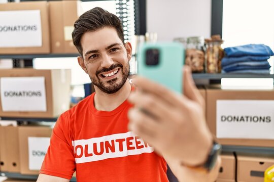 Young hispanic volunteer man making selfie by the smartphone working at charity center.