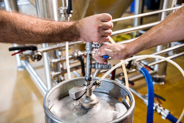 Young male brewer in leather apron supervising the process of beer fermentation at modern brewery factory