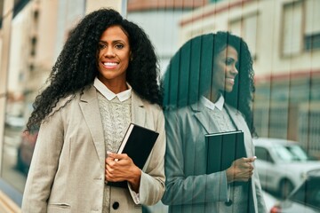 Middle age african american businesswoman smiling happy holding book at the city.