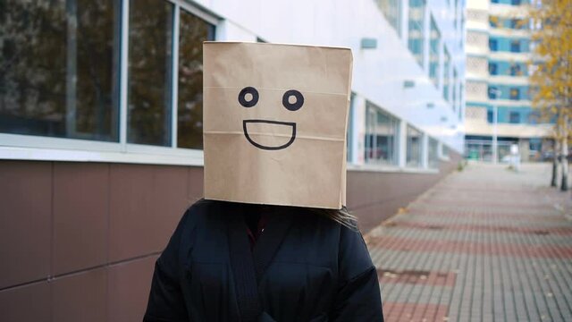 Smiling happy paper bag face walking along street. Funny woman wearing bread bag with pleased face
