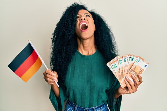 Middle age african american woman holding germany flag and euros banknotes angry and mad screaming frustrated and furious, shouting with anger looking up.