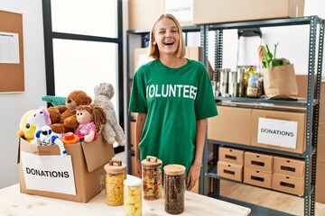 Young caucasian woman wearing volunteer t shirt at donations stand winking looking at the camera...