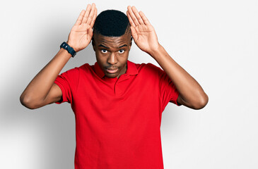 Young african american man wearing casual red t shirt doing bunny ears gesture with hands palms looking cynical and skeptical. easter rabbit concept.