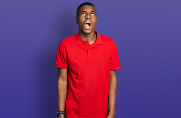 Young african american man wearing casual red t shirt angry and mad screaming frustrated and furious, shouting with anger. rage and aggressive concept.