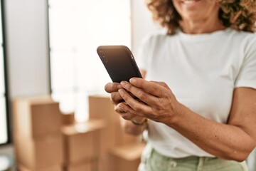 Naklejka premium Middle age hispanic woman smiling confident using smartphone at new home