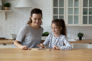 Happy caring beautiful young mother or babysitter playing draughts with little kid daughter,...