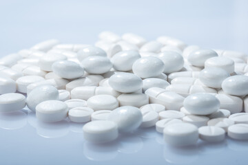 Closeup of white pills against white background. White pill container in the background.
