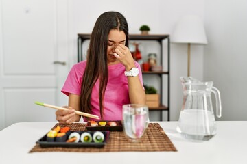 Young brunette woman eating sushi using chopsticks tired rubbing nose and eyes feeling fatigue and headache. stress and frustration concept.