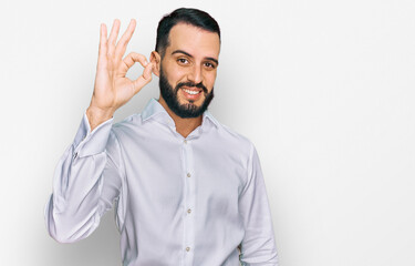 Young man with beard wearing business shirt smiling positive doing ok sign with hand and fingers. successful expression.