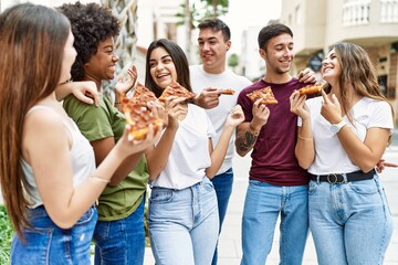 Group of young friends smiling happy eating pizza standing at the city.