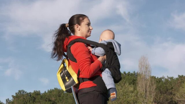 Travel with baby, mother carrying little baby with infant kid carrier on a walk outdoors, mom with six month baby boy in hipseat sling hiking in the mountains of Crimea, Russia High quality 4k footage