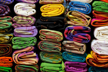 Artistic variety shade tone colors ornaments patterns, closeup view of stacked saris or sarees in display of retail shop.