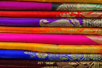 Artistic variety shade tone colors ornaments patterns, closeup view of stacked saris or sarees in...