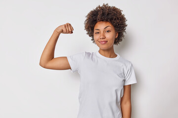 Confident woman feels strength and power raises arm flexes biceps and looks proud of her own...