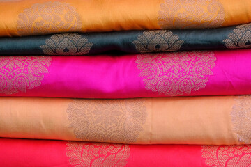 Artistic variety shade tone colors ornaments patterns, closeup view of stacked saris or sarees in display of retail shop.
