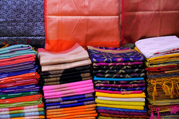 Artistic variety shade tone colors ornaments patterns, closeup view of stacked saris or sarees in display of retail shop, Copy Space.
