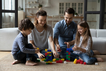 Happy young parents couple playing toys with joyful small kids siblings, spending stress free...