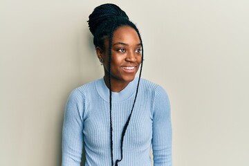 Fototapeta premium African american woman with braided hair wearing casual blue sweater looking to side, relax profile pose with natural face and confident smile.