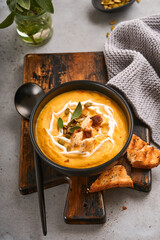Pumpkin traditional soup with creamy silky texture with sage leaves and red pepper in black plate or bowl. Old grey background. Copy space. Mock up. Top view, flat lay.