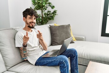 Hispanic man with beard sitting on the sofa pointing fingers to camera with happy and funny face. good energy and vibes.