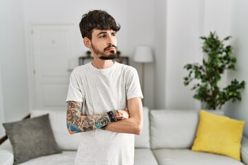 Hispanic man with beard at the living room at home looking to the side with arms crossed convinced and confident