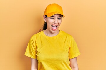 Young hispanic woman wearing delivery uniform and cap winking looking at the camera with sexy...