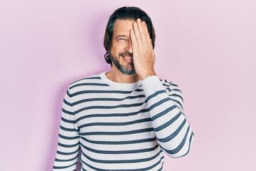 Middle age caucasian man wearing casual clothes covering one eye with hand, confident smile on face and surprise emotion.