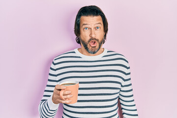 Fototapeta premium Middle age caucasian man drinking a cup of coffee scared and amazed with open mouth for surprise, disbelief face