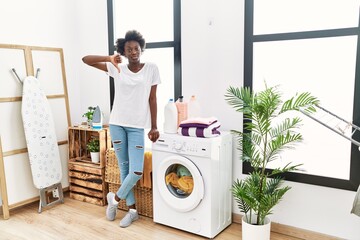 African young woman doing laundry at home with angry face, negative sign showing dislike with...