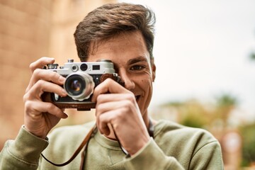 Fototapeta premium Young hispanic tourist man smiling happy using vintage camera at the city.