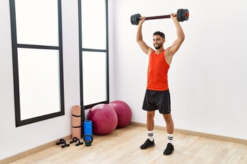 Fototapeta na wymiar Young arab man smiling confident training with dumbbells at sport center