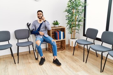 Fototapeta premium Young arab man injured smiling confident talking on the smartphone at clinic waiting room